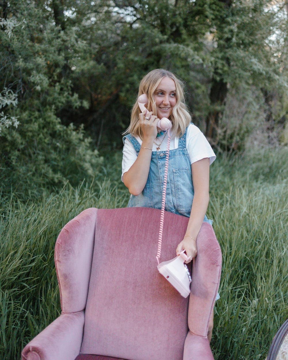 Brooklyn standing behind a pink velvet chair, phone in hand