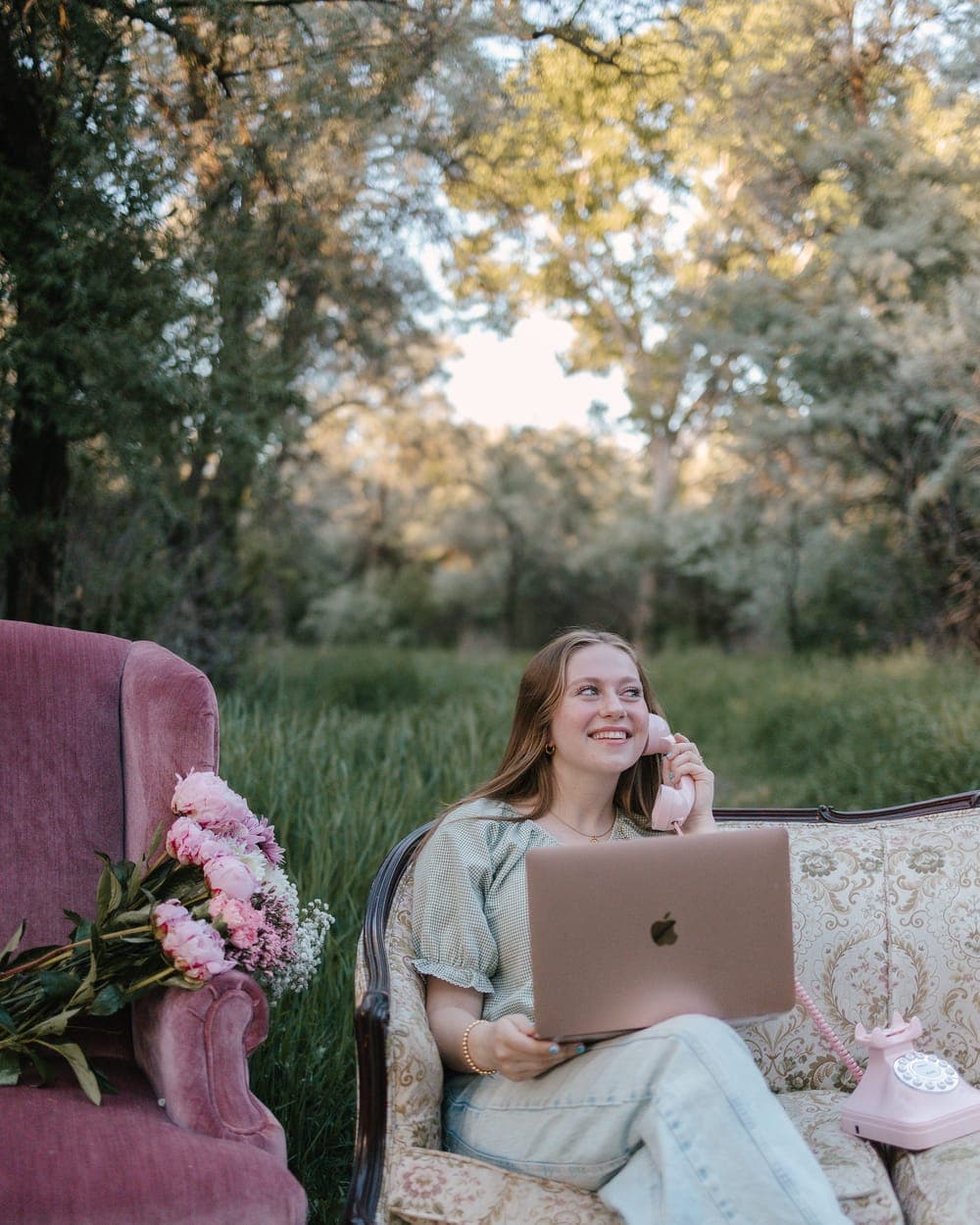 Emma on a rotary phone with a laptop, sitting on a floral couch outdoors