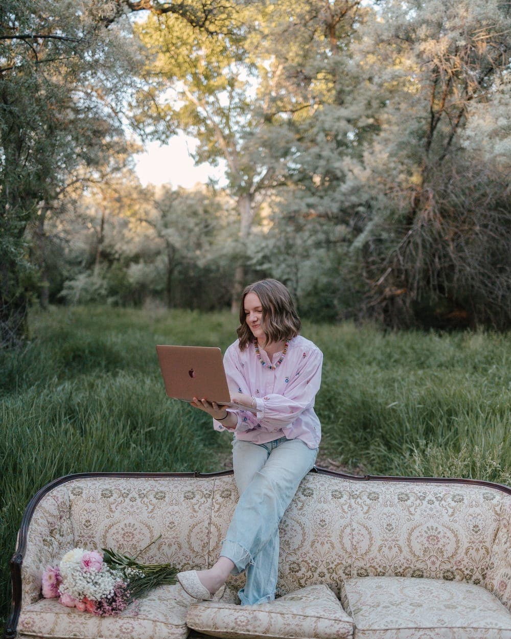 Krista working on a laptop while perched on a vintage couch in a field