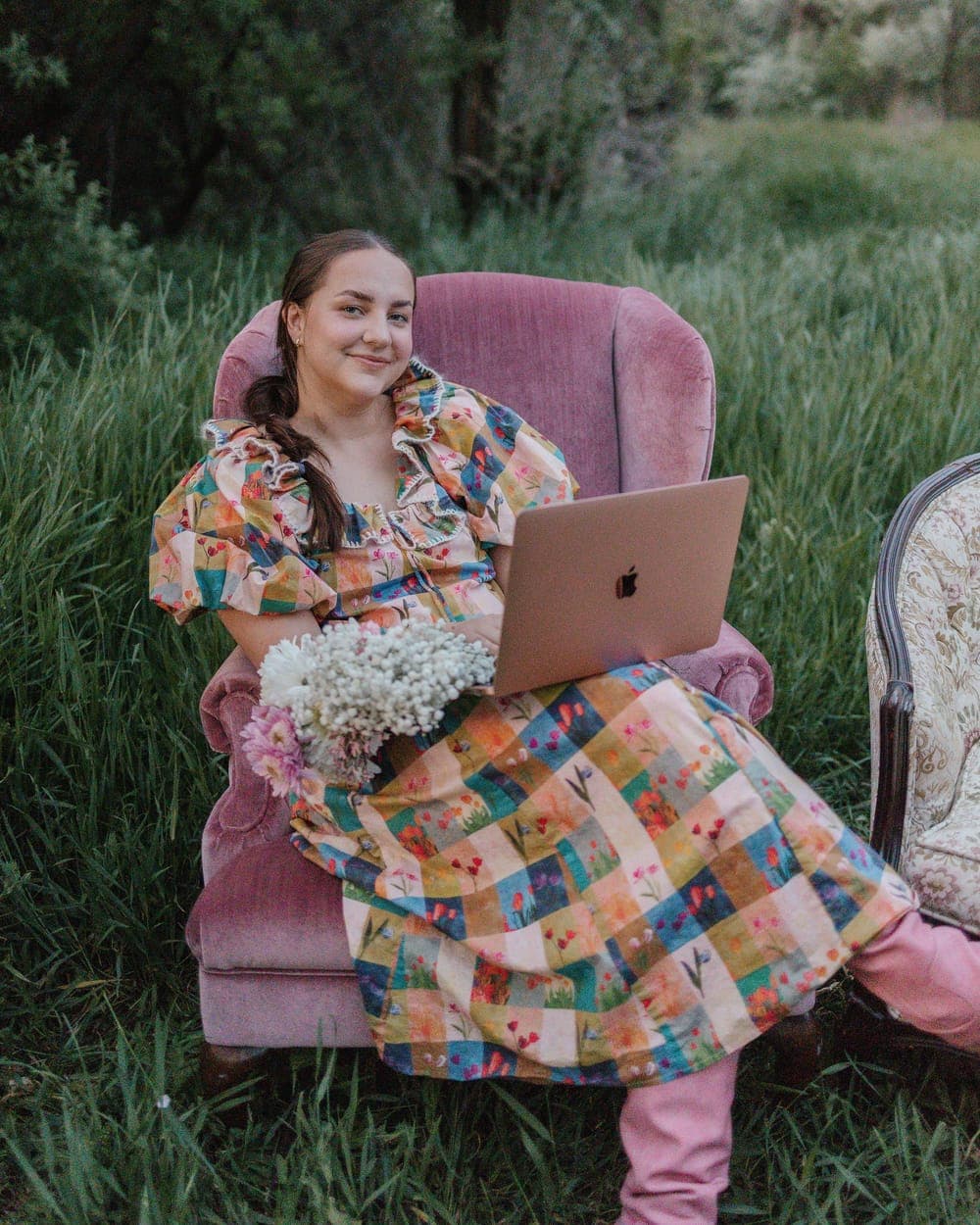 Sydney in a pink armchair with a laptop and a bouquet of flowers