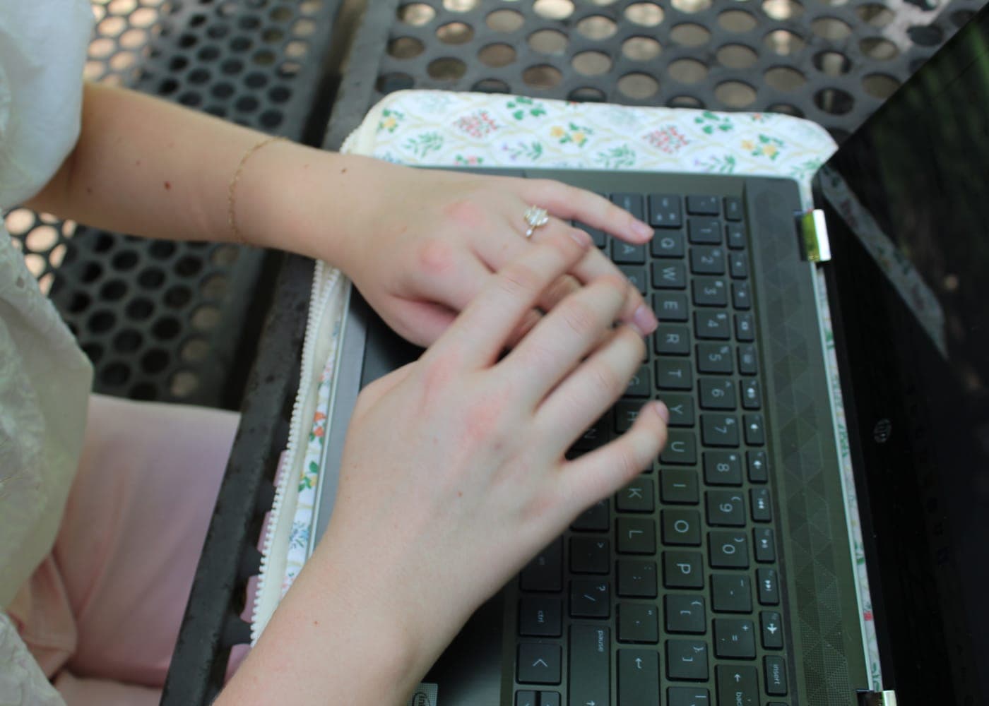 Close-up of hands typing on a laptop with a floral cover at a picnic table